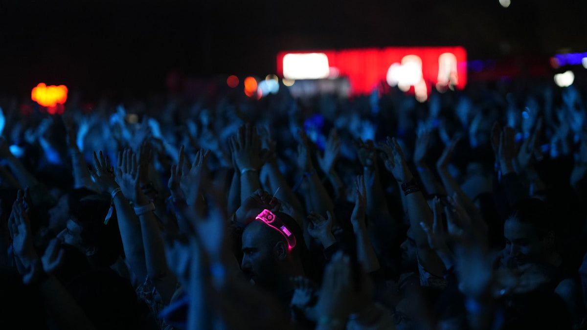 A dense concert crowd with raised hands under blue light