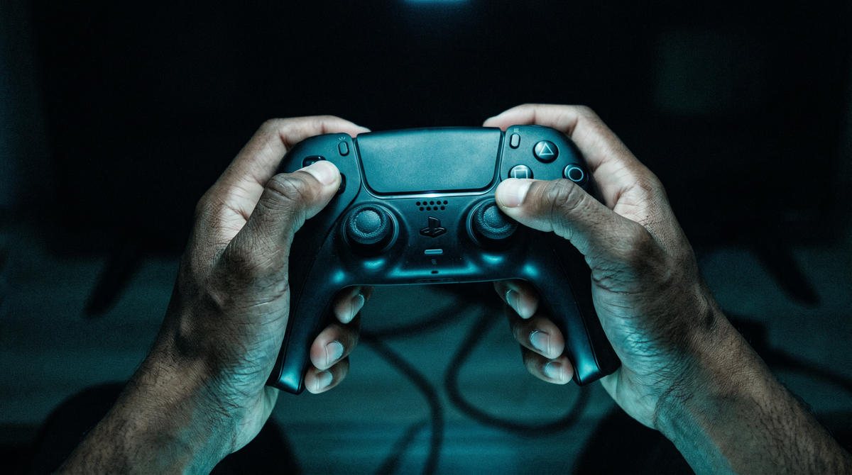Two hands gripping a game controller in a dark room lit by a teal glow