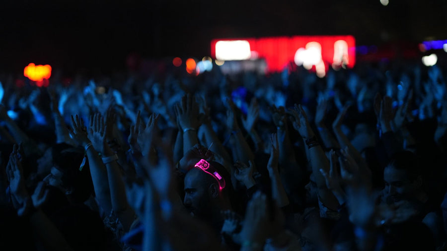 A dense concert crowd with raised hands under blue light