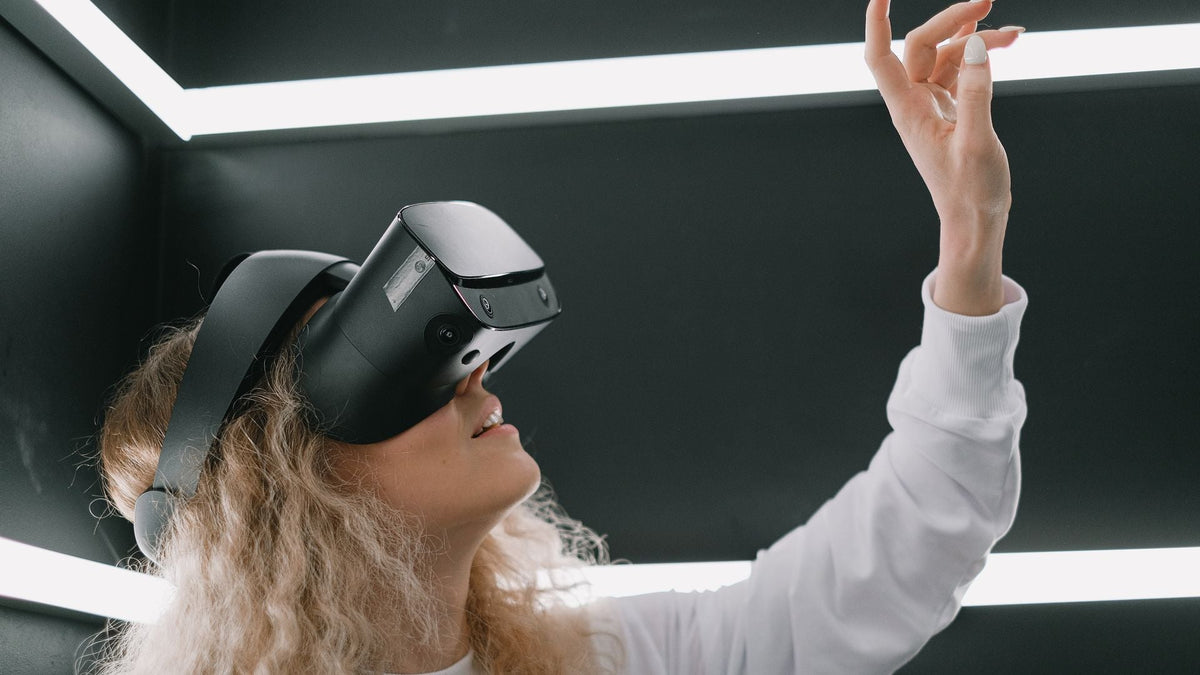 A woman in a VR headset reaching up toward a light in a bright room